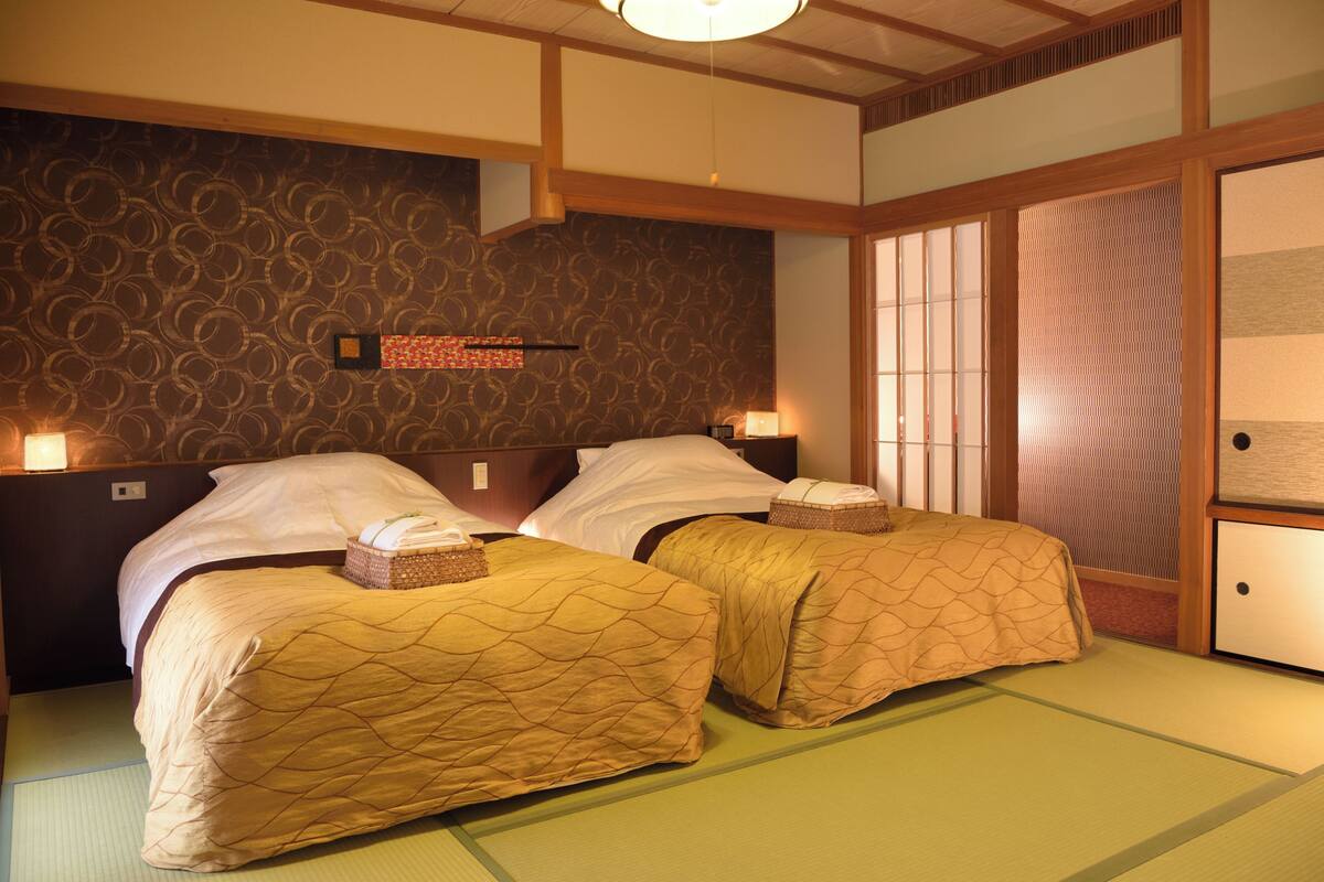 Ein traditioneller japanischer Raum mit Tatami-Boden, zwei Betten mit passendem Bettzeug, einer Shoji-Schiebetür und einer Wand mit einem kreisförmigen Muster.