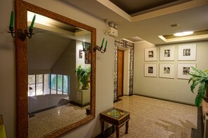 Un couloir orné d’un grand miroir décoratif, une petite table sur laquelle est posé un objet décoratif, et des tableaux encadrés accrochés au mur.