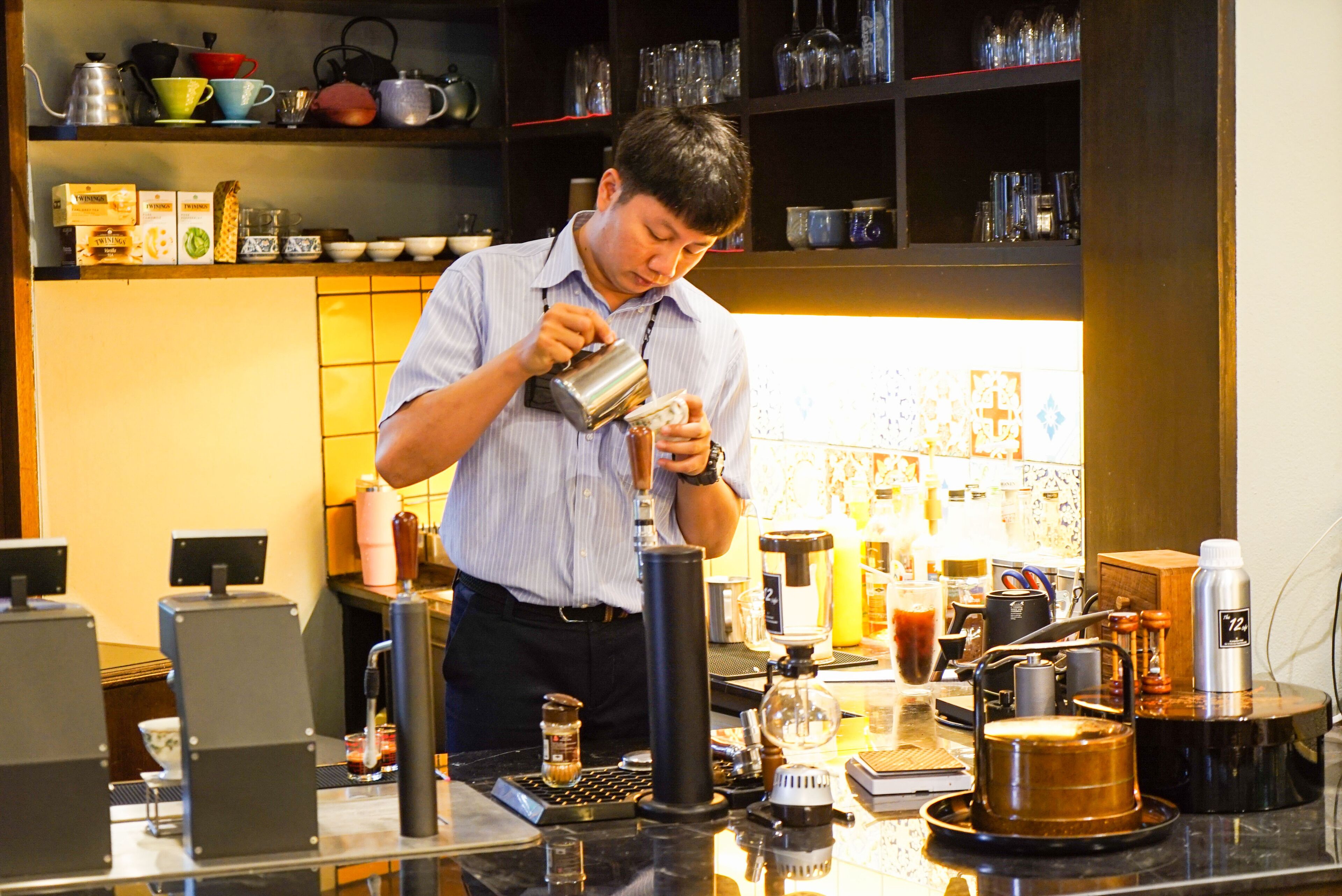 Un barista prépare une boisson à un comptoir où se trouvent divers appareils et récipients pour préparer le café.