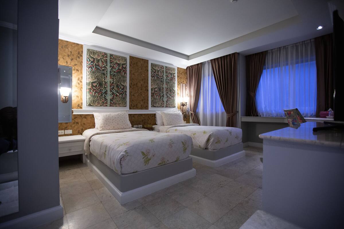 Habitació d'hotel amb dos llits, una taula de treball, un mirall i una finestra amb cortines.