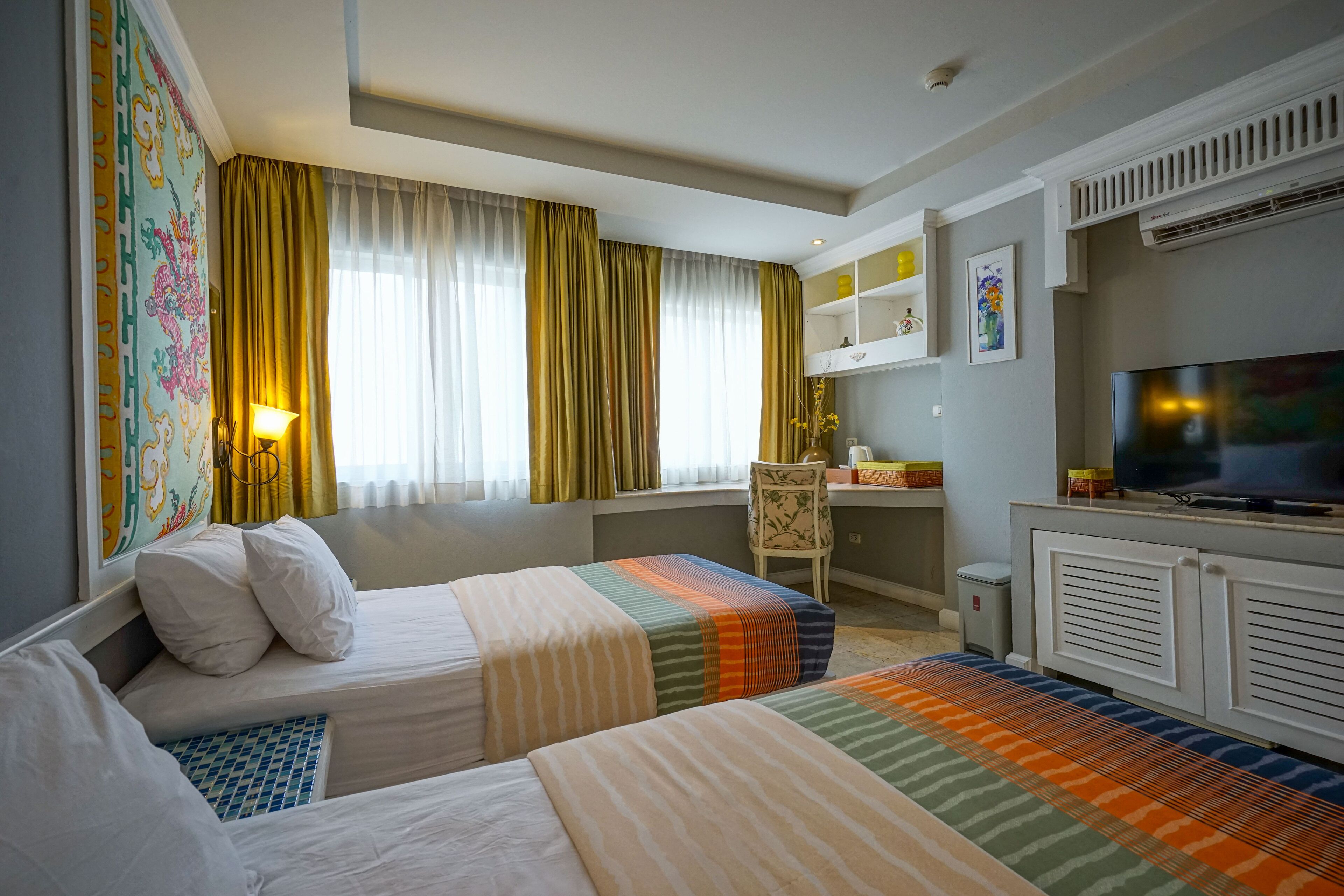 Quarto de hotel com duas camas, uma escrivaninha, uma cadeira, uma televisão e uma janela com cortinas.