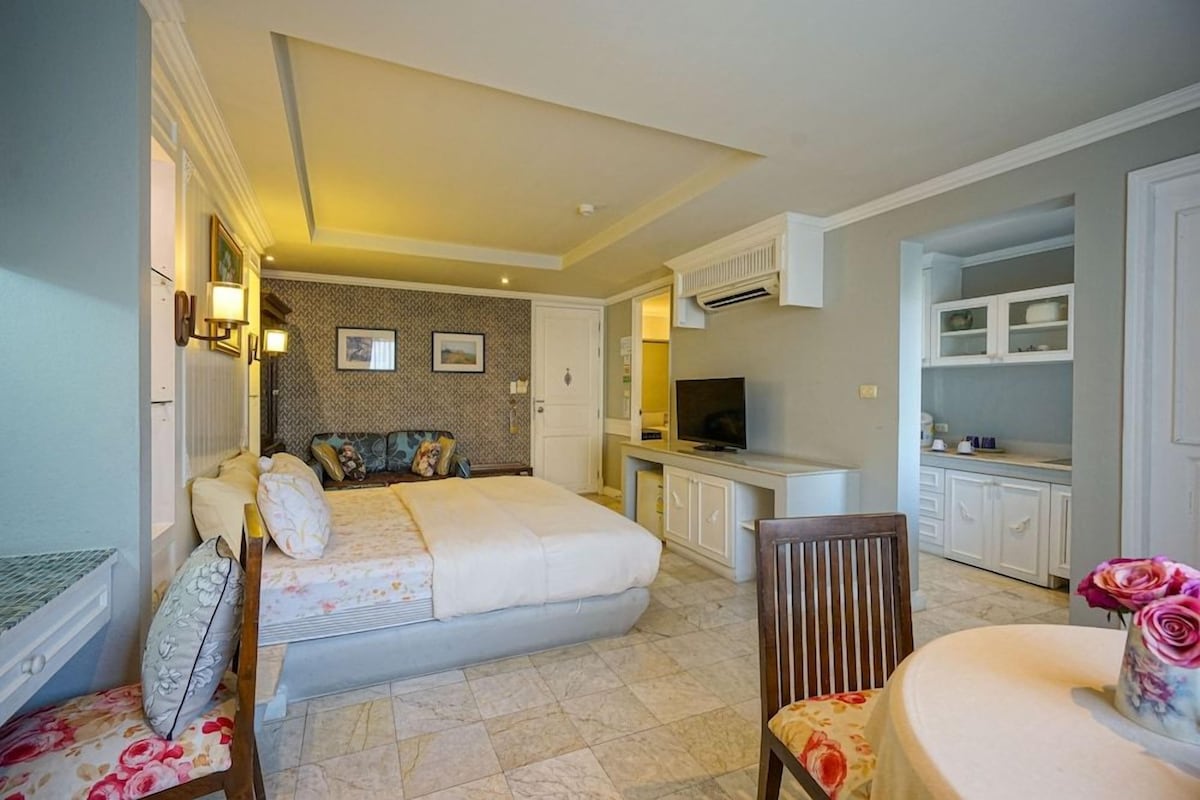 Ein gemütliches Schlafzimmer mit Bett, Stuhl, kleinem Tisch, Fernseher und einer Küchenzeile.