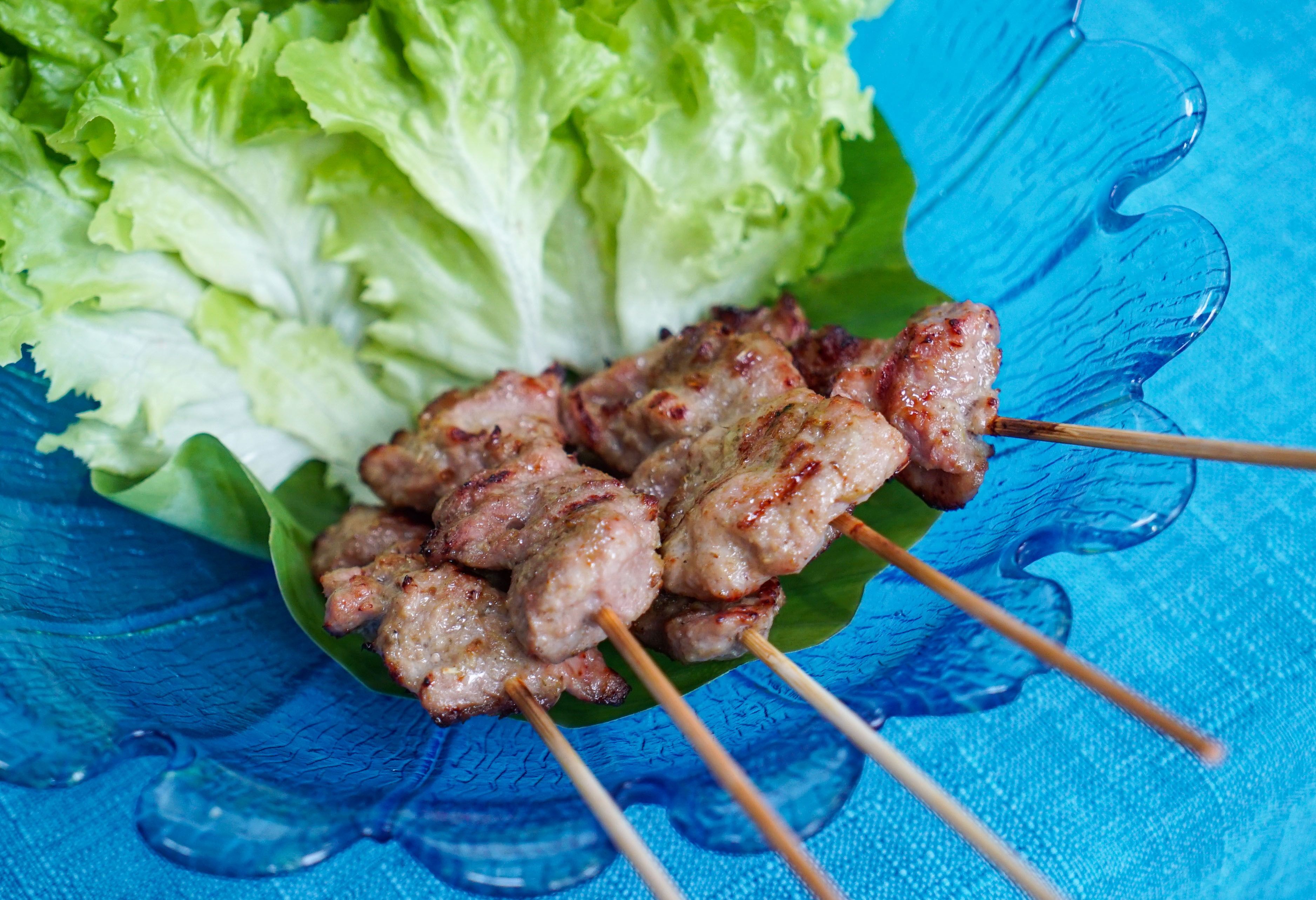 Skewers of grilled meat on a blue glass plate with lettuce leaves.