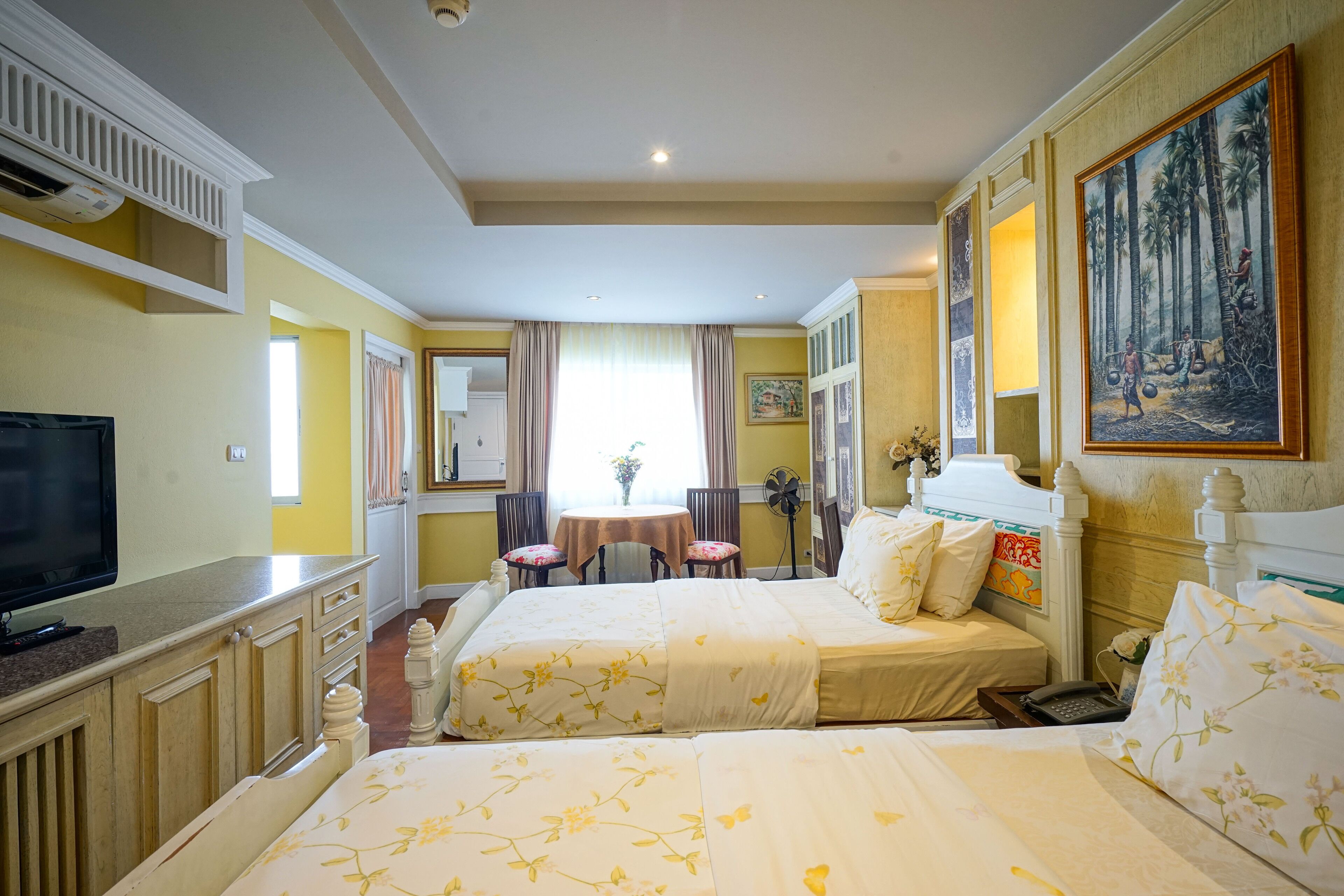 A hotel room with two beds, a TV, a desk, and a dining area with chairs and a table.