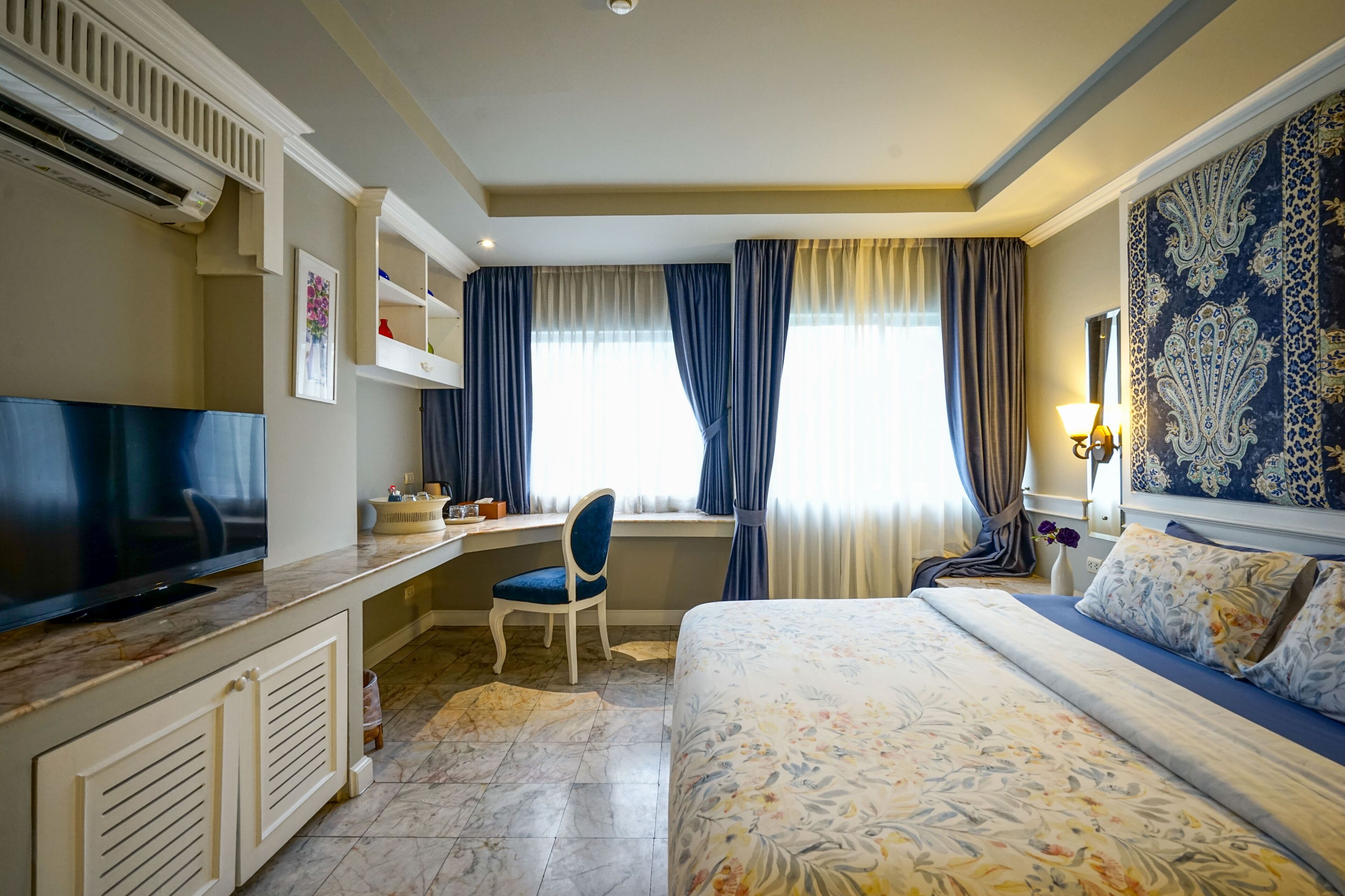 A hotel room with a bed, a desk with a chair, a television, and a window with curtains.