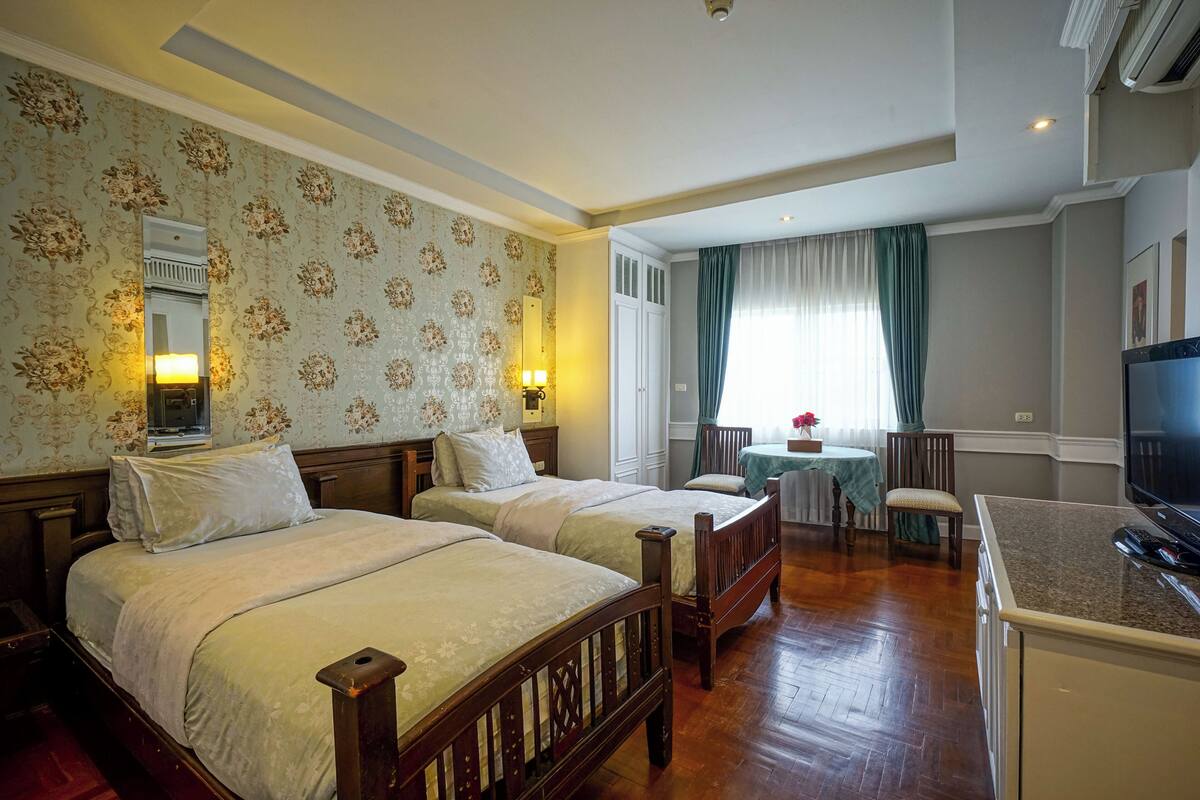 Habitació d'hotel amb dos llits de fusta, una petita zona de menjador i una televisió.