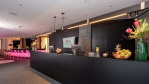 Zona de recepción de hotel con diseño moderno, que incluye un mostrador de recepción, un área de descanso y una pantalla grande que muestra el nombre del hotel.