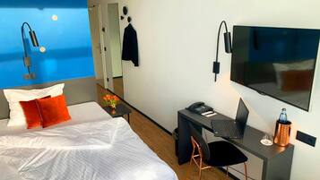 Une chambre d’hôtel moderne équipée d’un lit, d’un bureau avec un ordinateur portable, d’une chaise, d’une télévision et d’un miroir.