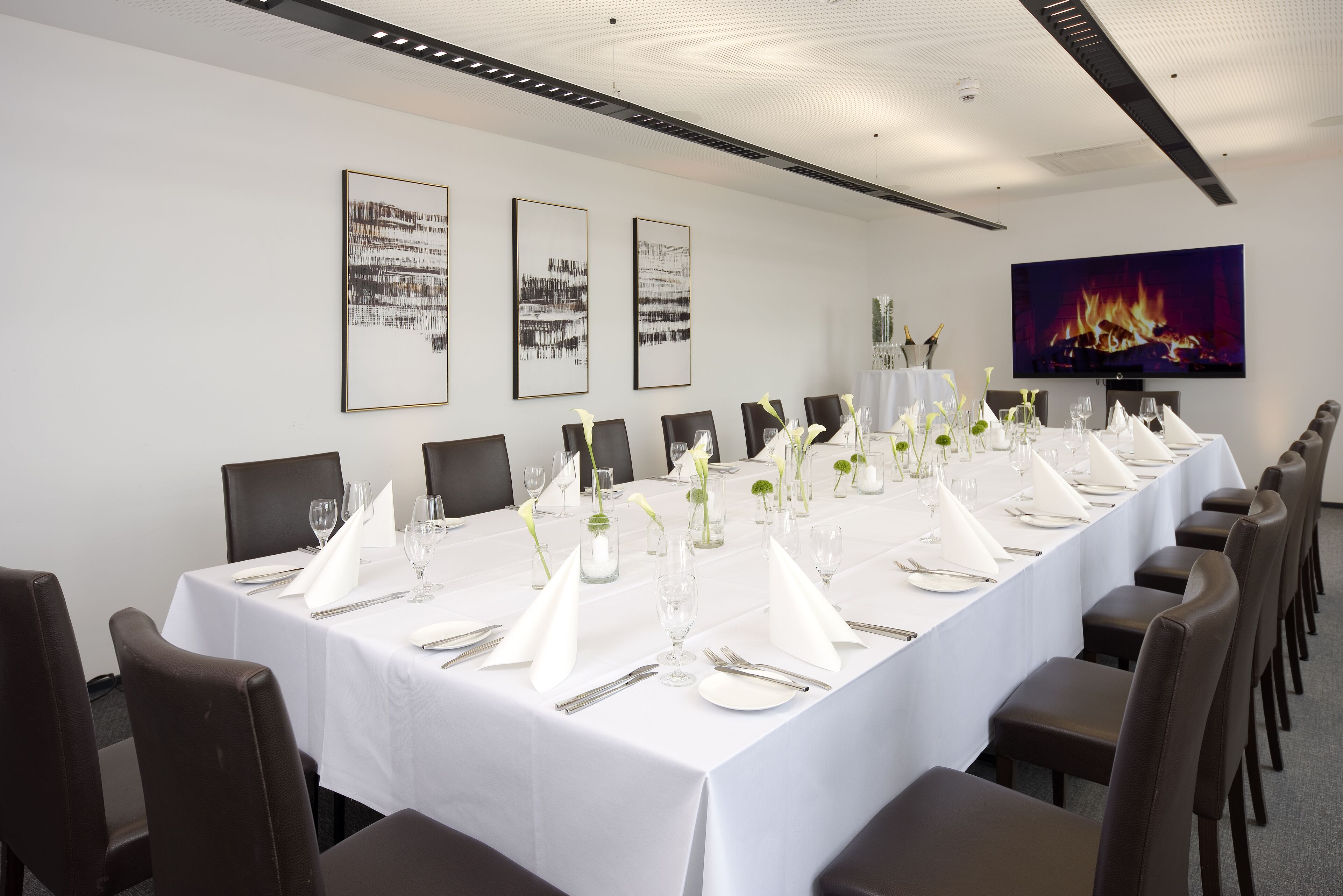 Una larga mesa de comedor preparada para un evento formal, con manteles blancos, cubiertos y copas.