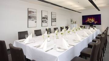 Una larga mesa de comedor preparada para un evento formal, con manteles blancos, cubiertos y copas.