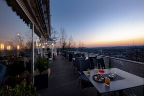 An outdoor dining area with tables and chairs, overlooking a cityscape at sunset. - Schlossberg Hotel Homburg (Homburg)
