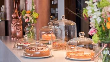 Una presentación de postres con diversos pasteles bajo campanas de cristal, rodeada de arreglos florales.