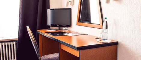 A hotel room with a wooden desk, a chair, a television, a mirror, and a radiator.