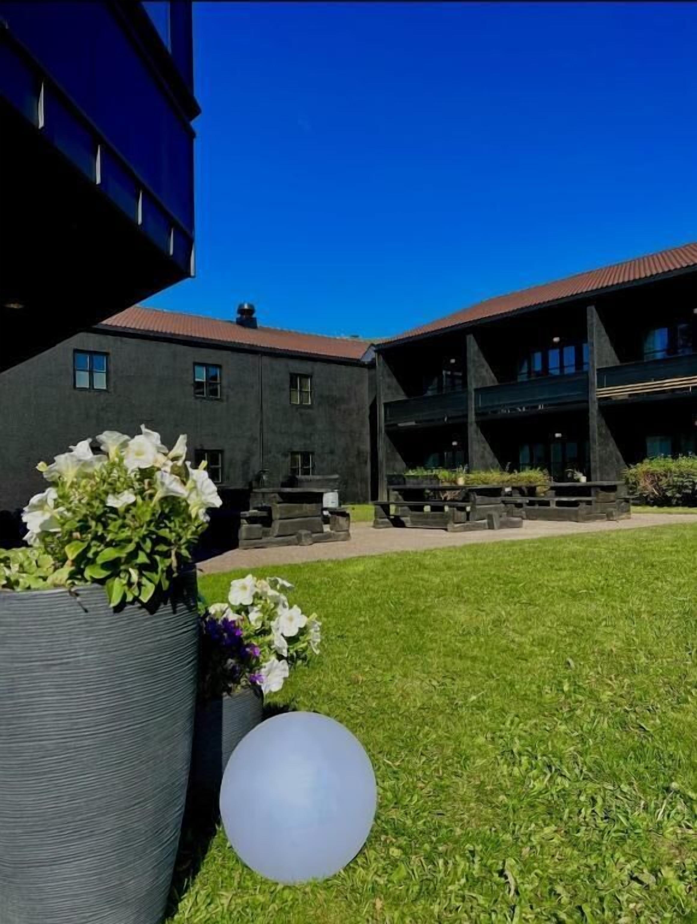 A courtyard with a building, potted plants, and a spherical object.