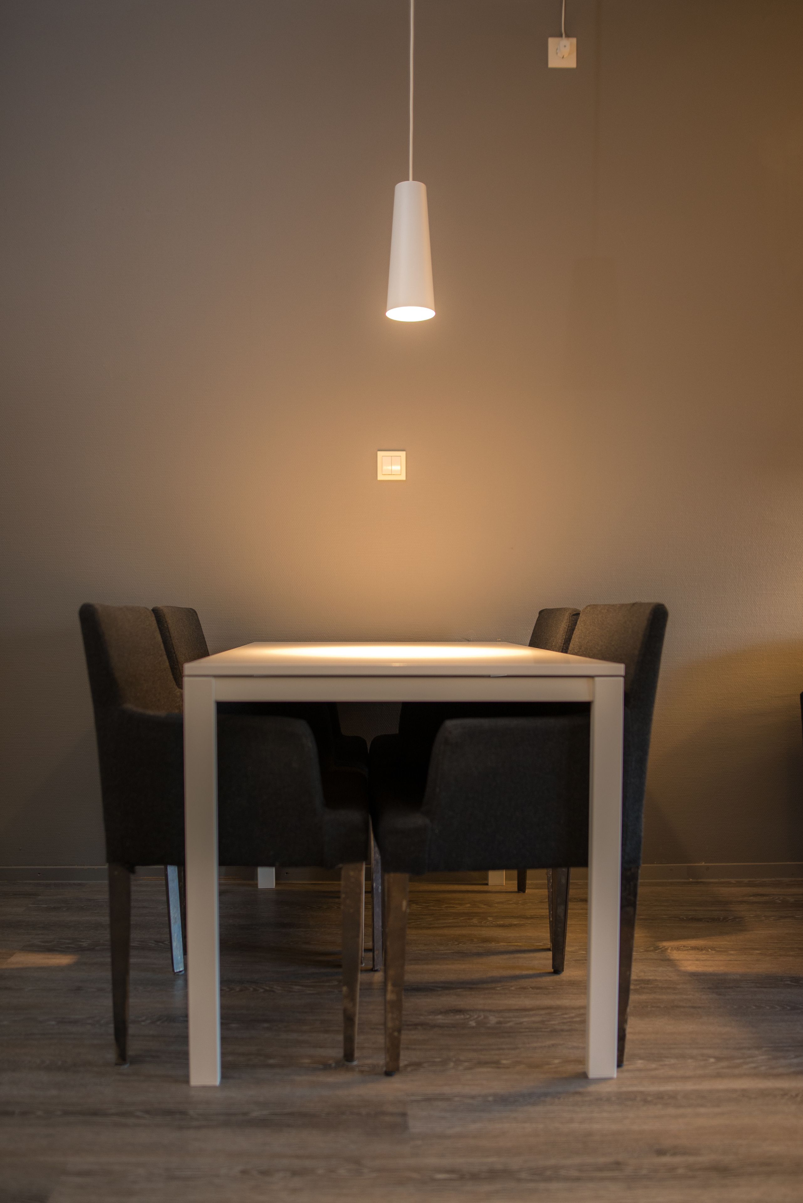 A dining area with a rectangular table and four chairs, a hanging pendant light, and a light switch on the wall.