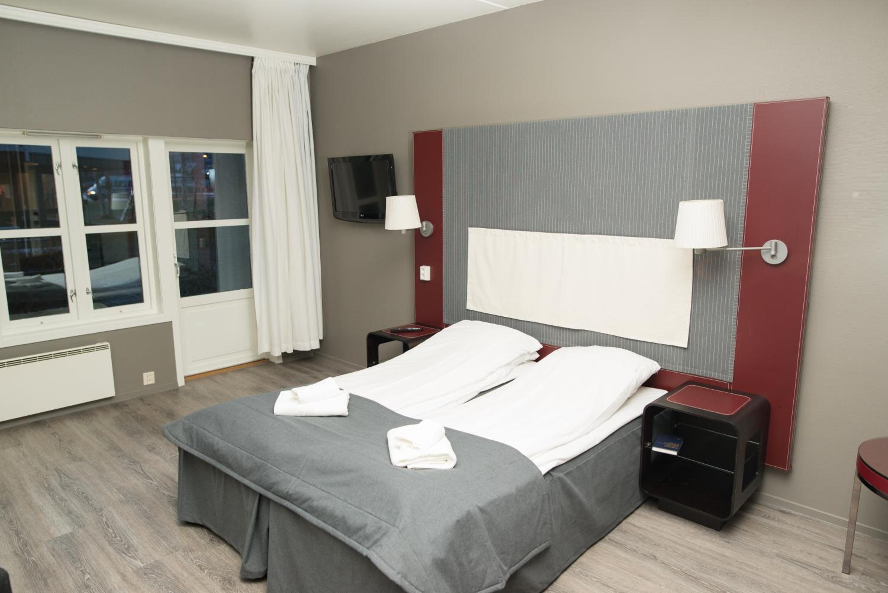 Een hotelkamer met een bed, twee nachtkastjes, een televisie en een raam met gordijnen.