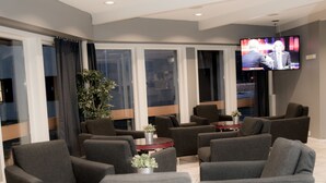 Un área de estar moderna con sofás grises, un televisor de pantalla plana y ventanas amplias.