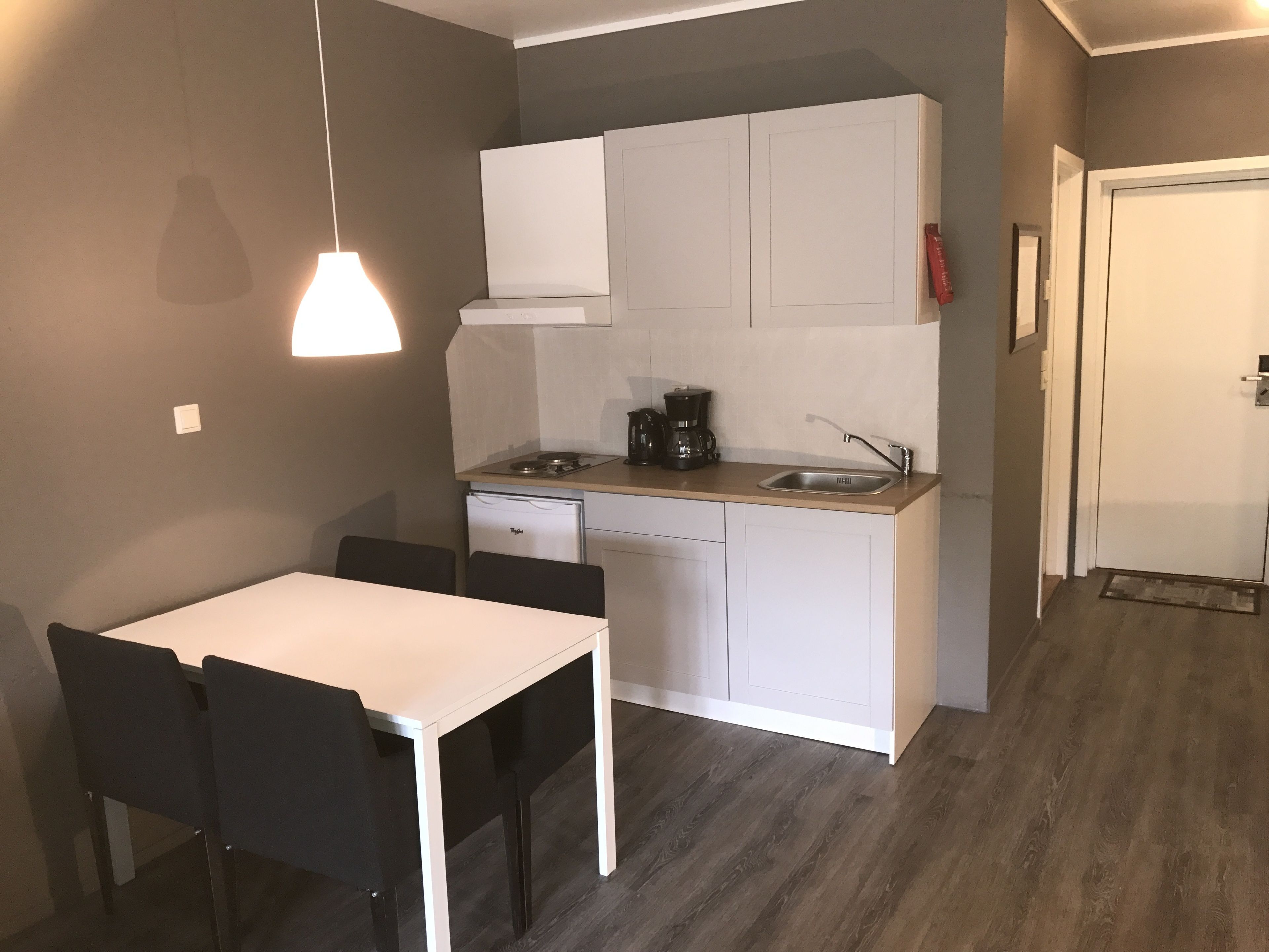 Una cocina compacta con muebles blancos, cafetera y lavamanos.