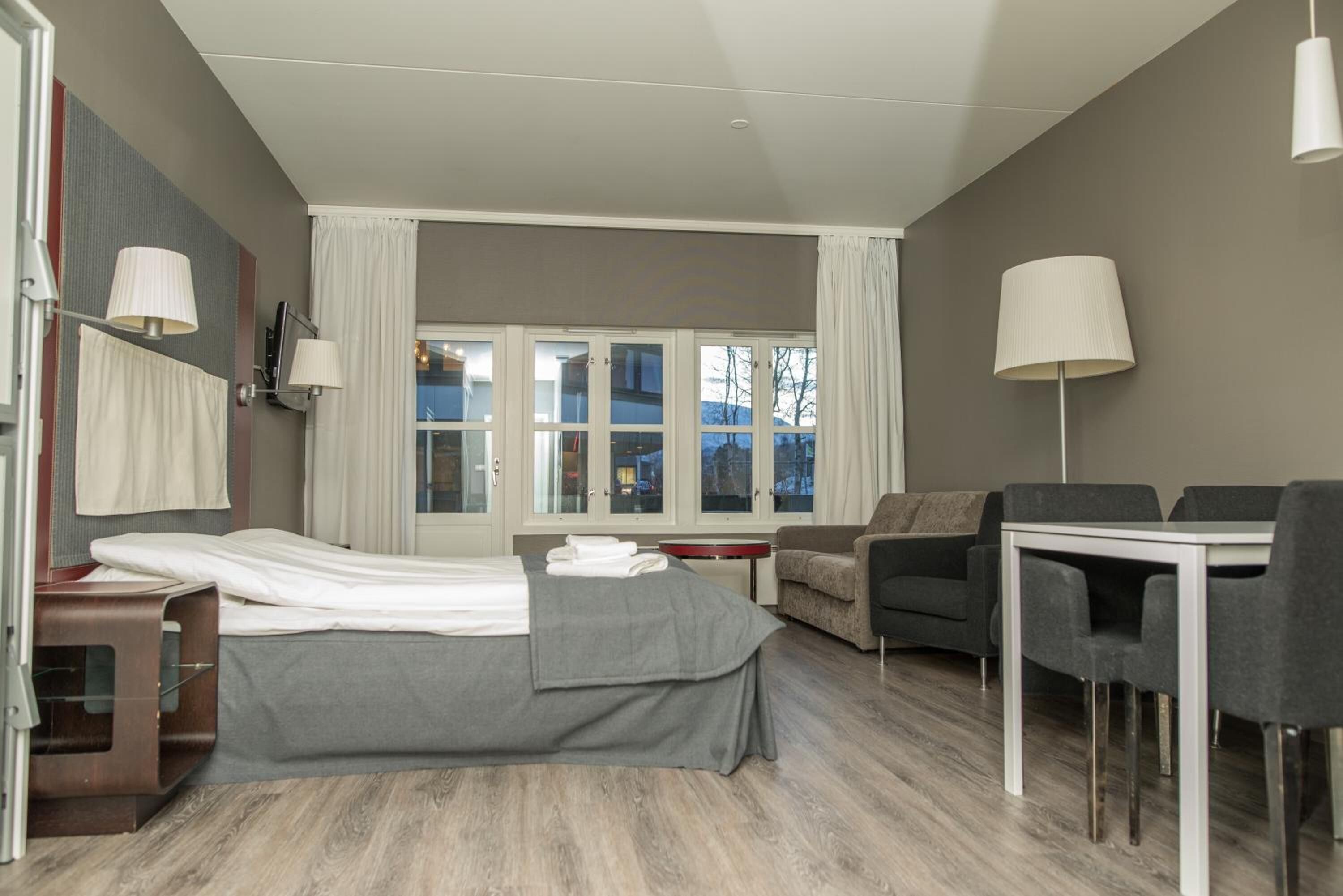 Una habitación de hotel moderna con cama, escritorio, sofá y mesa de comedor.