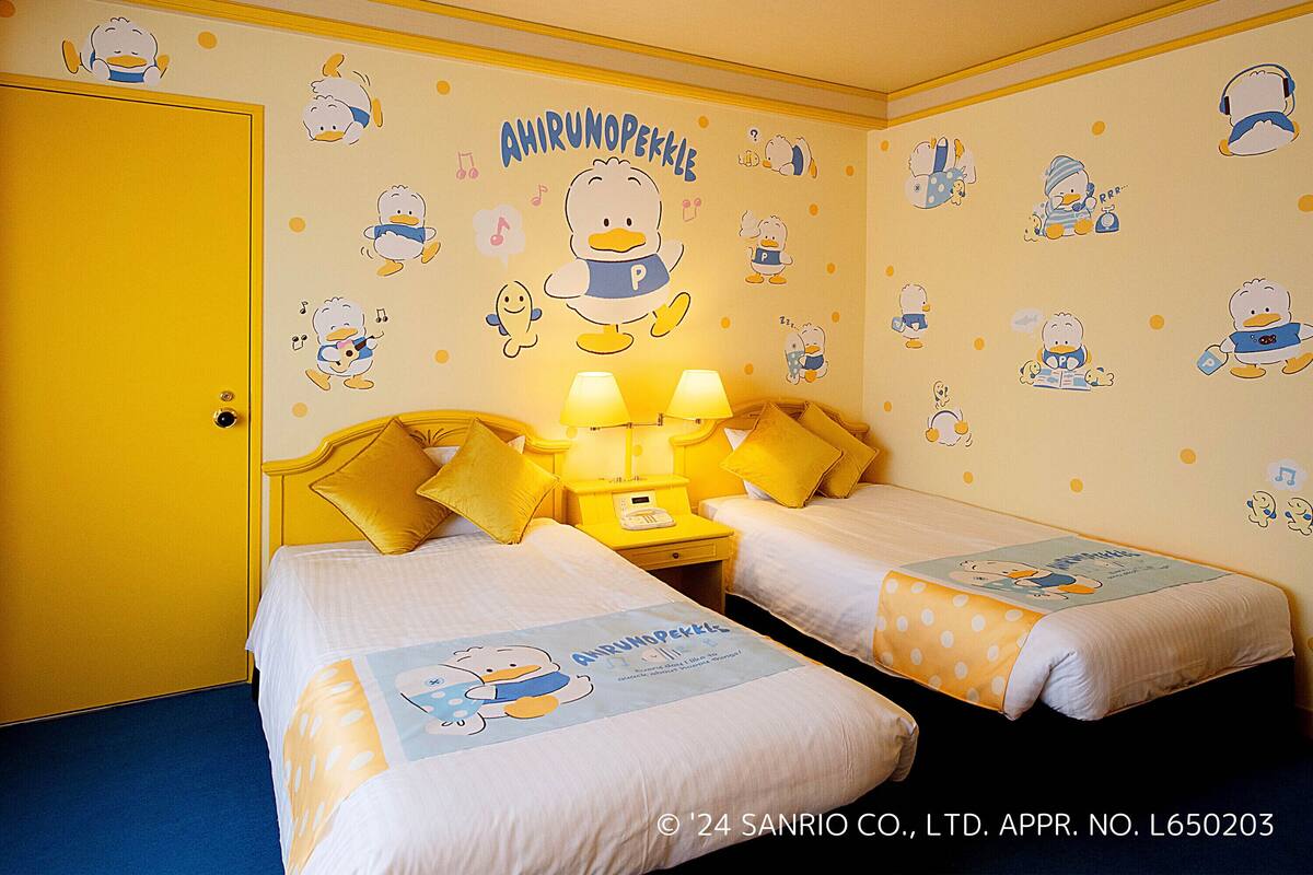 A children's room with two beds, yellow pillows, and wall decals of cartoon ducks.