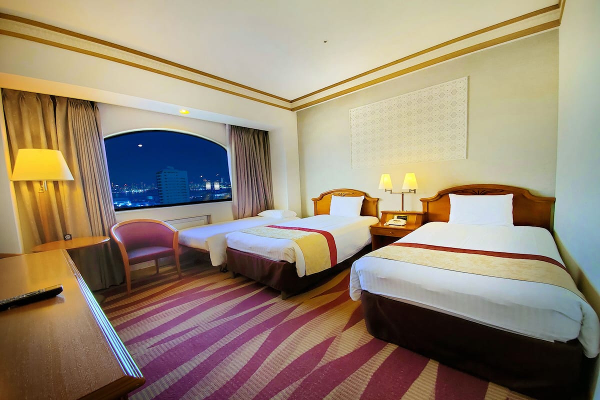 A hotel room with two beds, a desk, a chair, and a view of the city at night.