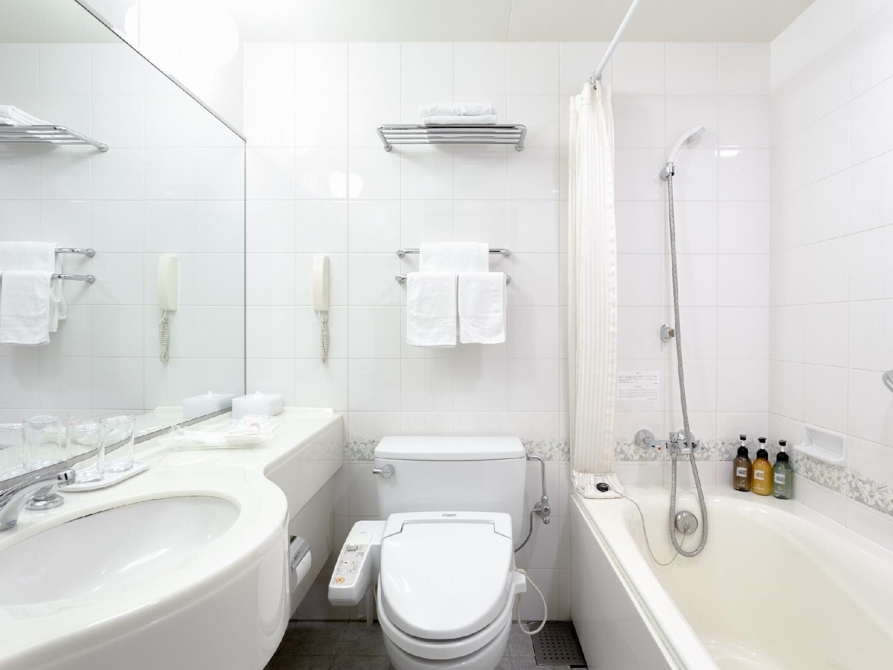 A modern bathroom with a white sink, toilet, and bathtub. There are two towel racks, a showerhead, and a toilet paper holder.