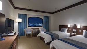 Habitación de hotel con dos camas, un escritorio con silla, televisor y vista a la ciudad de noche.