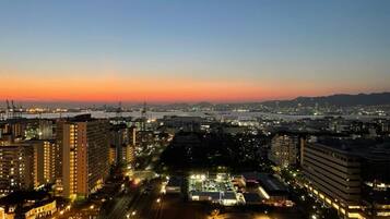A cityscape at dusk with high-rise buildings, a river, and a bridge.
