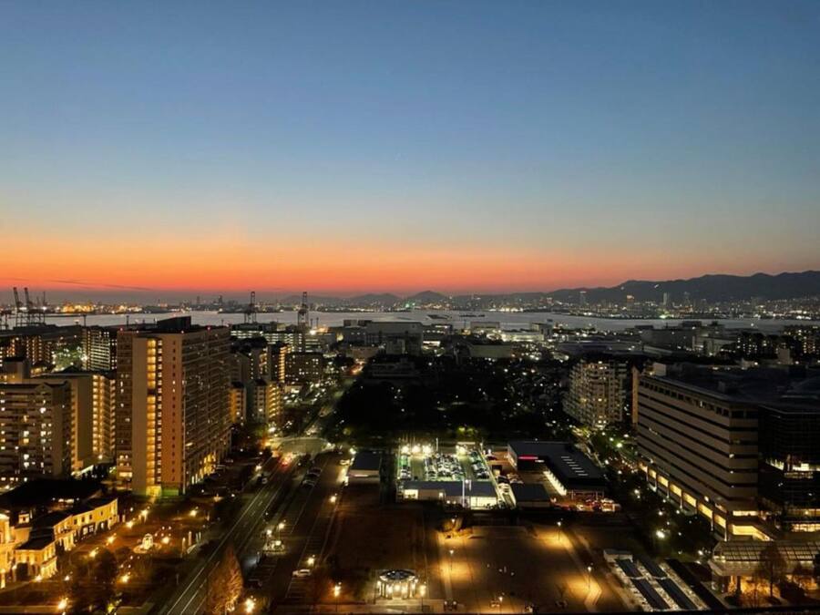 A cityscape at dusk with high-rise buildings, a river, and a bridge.