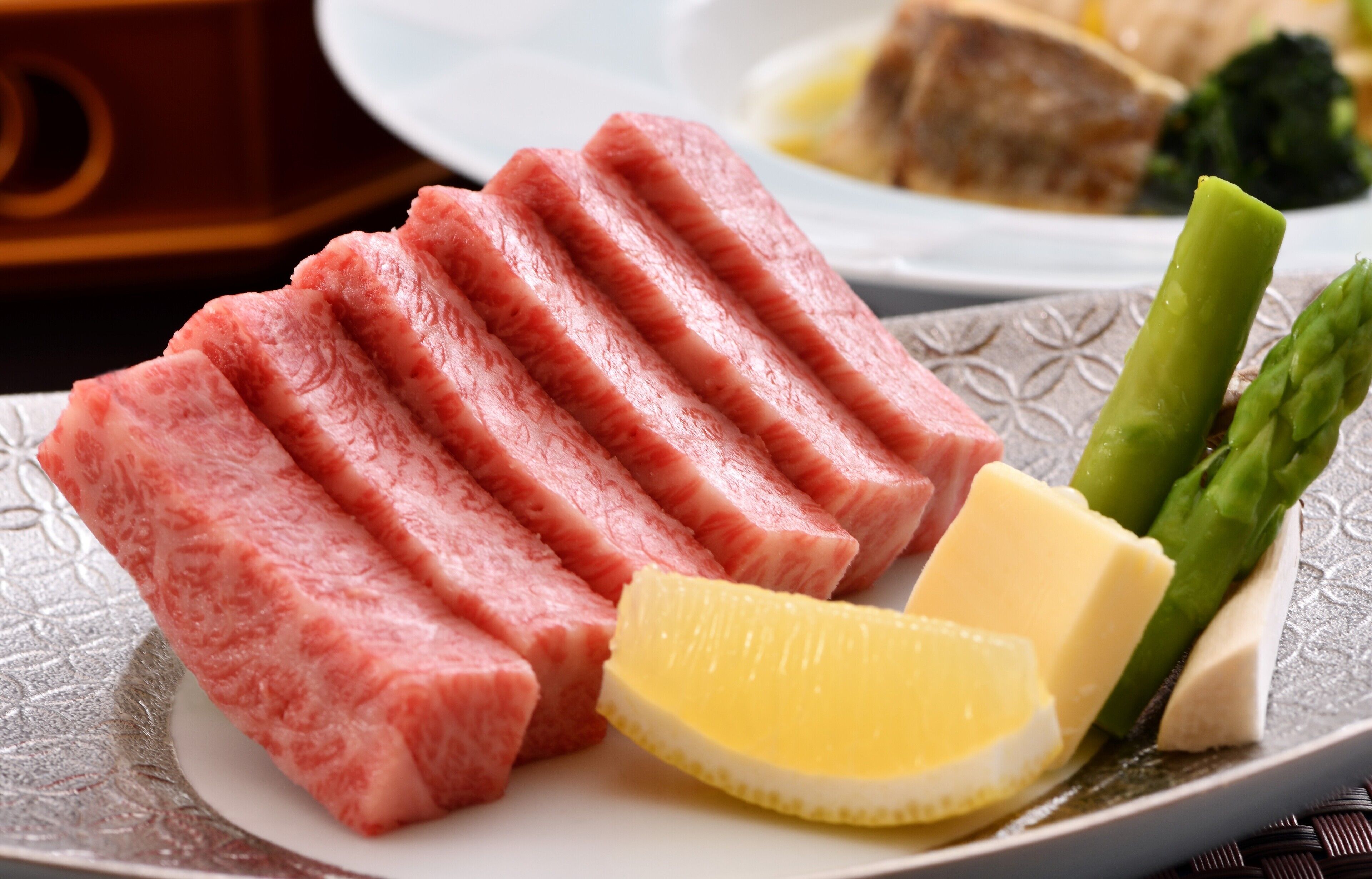 Une assiette contenant de la viande tranchée, des asperges et des quartiers de citron.