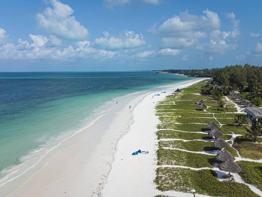 A beach resort with a long sandy shoreline, thatched-roof huts, and lush greenery.