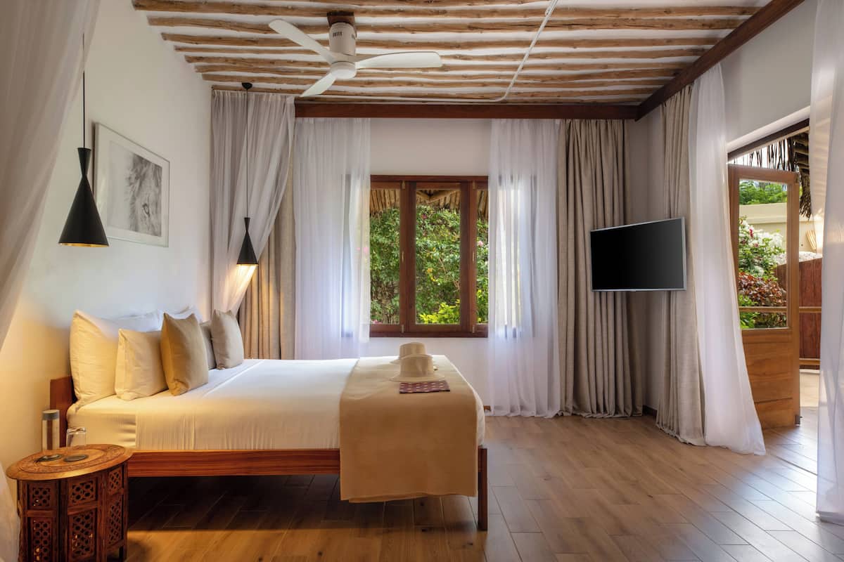 A bedroom with a wooden bed, a bedside table, a TV, and a window with curtains.