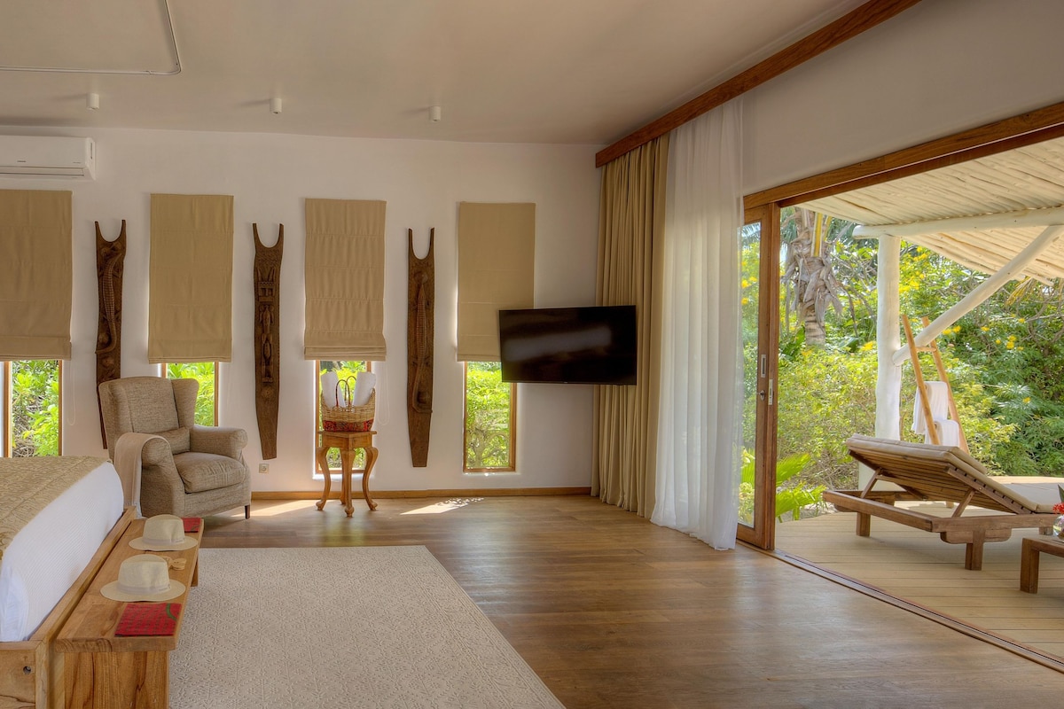 A bedroom with a bed, a chair, a TV, and a view of the outdoors.