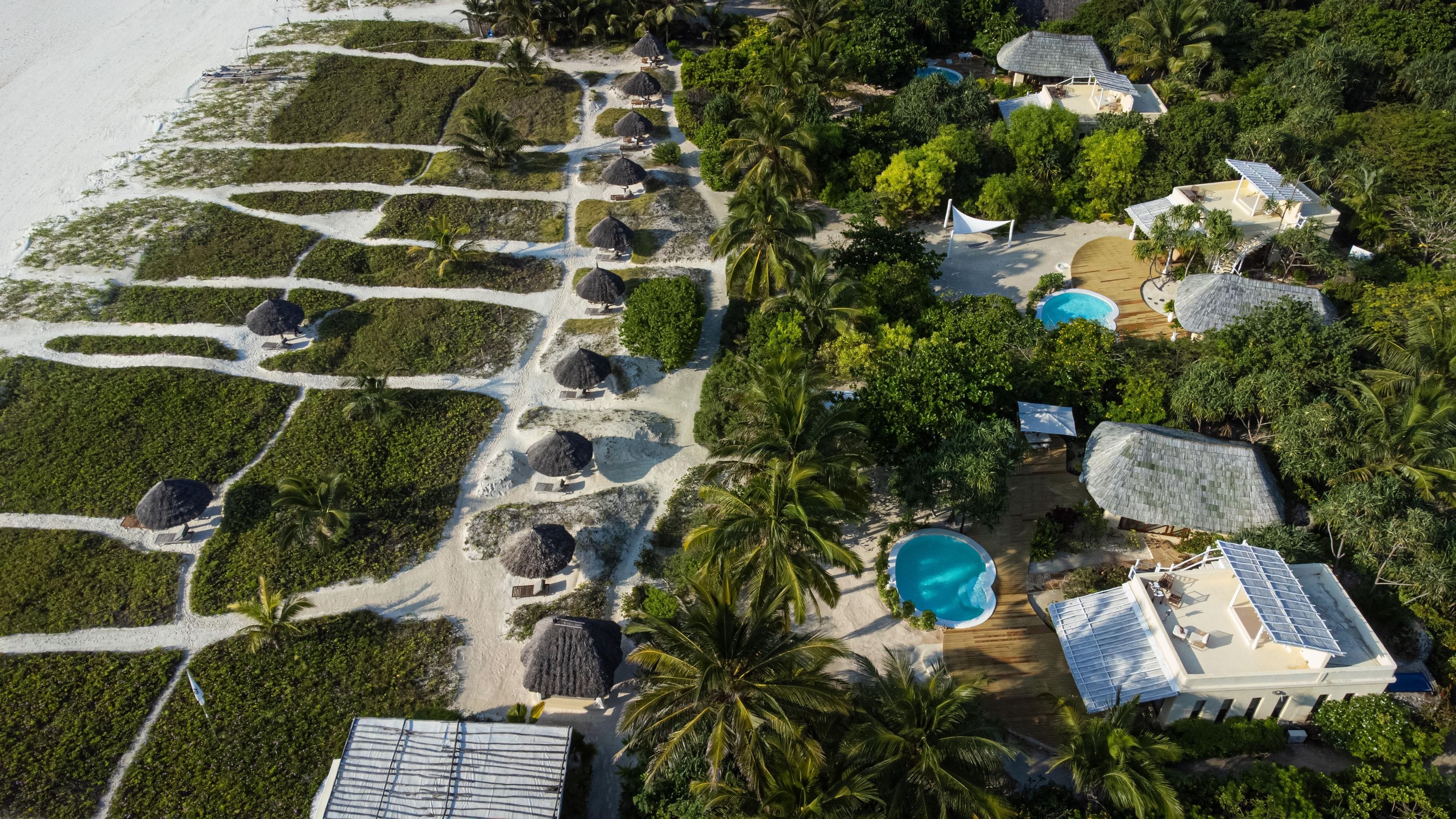 An aerial view of a resort with multiple swimming pools, thatched-roof structures, and lush greenery.