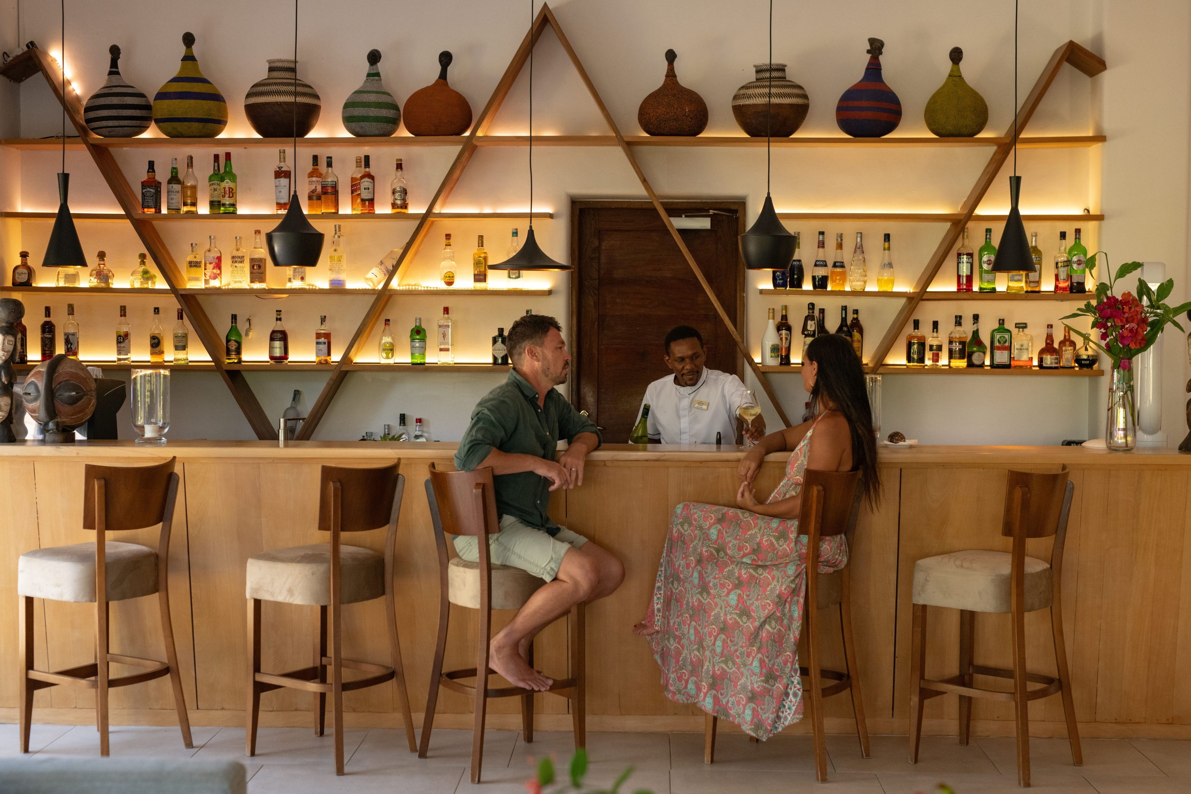 Una zona de bar con sillas de madera, una barra y estantes llenos de botellas.