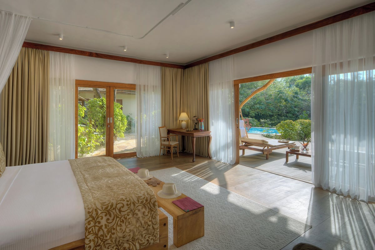 A spacious bedroom with a large bed, a desk, and a view of a pool and greenery.