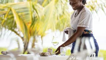 Una persona preparando una mesa con manteles blancos y cristalería, con palmeras al fondo y un ambiente tropical.
