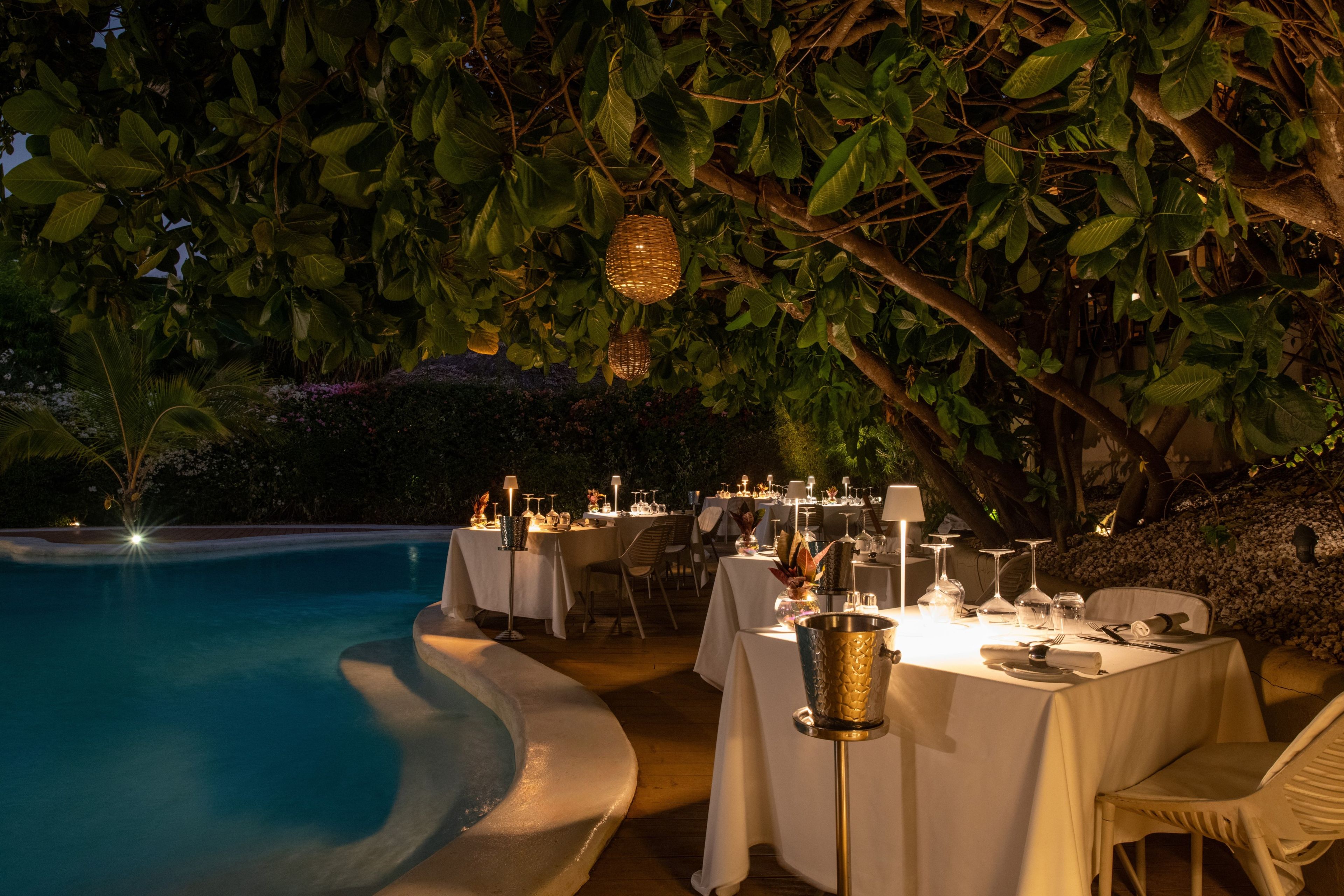 Un espacio de comedor al aire libre con mesas dispuestas para una comida, con vista a una piscina.