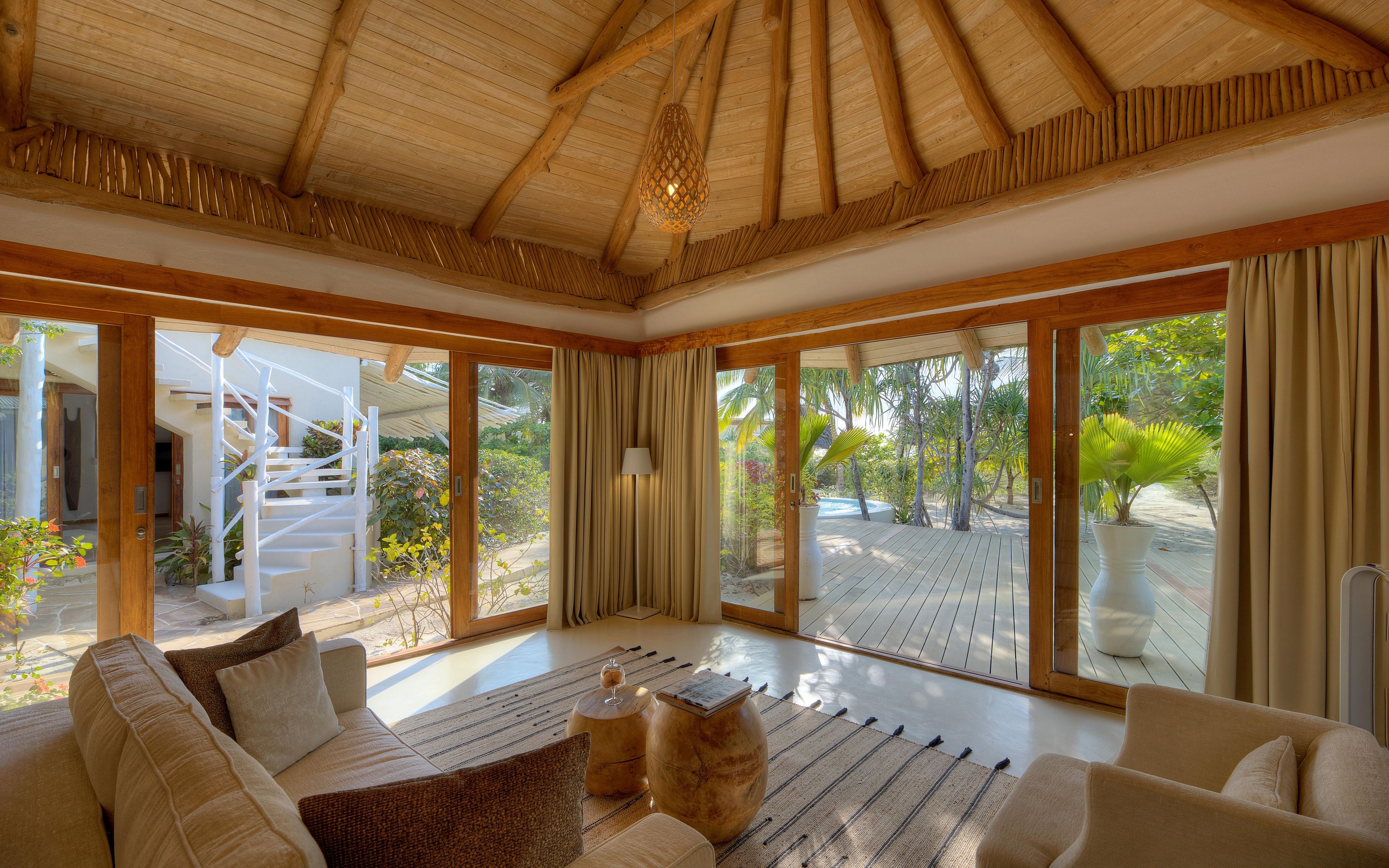 A spacious room with a wooden ceiling, large sliding glass doors leading to a deck, and a sofa with a woven rug.