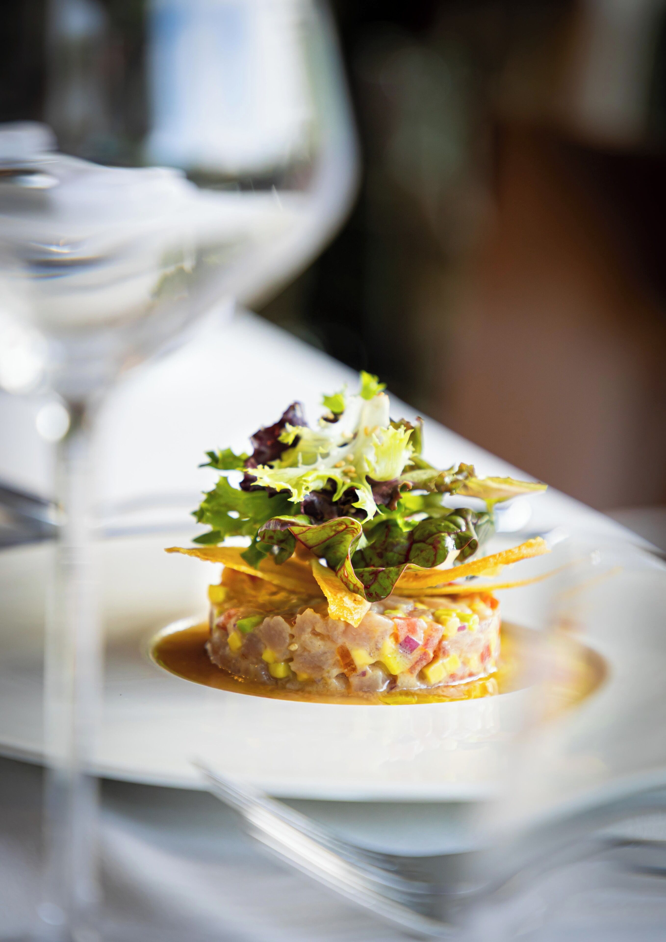 A plated dish with a garnish, a glass of white wine, and a blurred background.