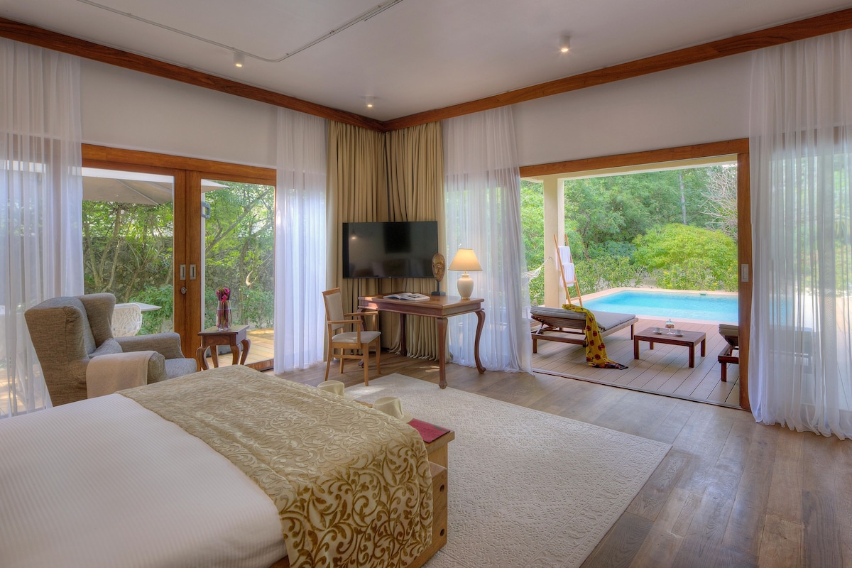 A bedroom with a large bed, a desk, a TV, and a view of a swimming pool.