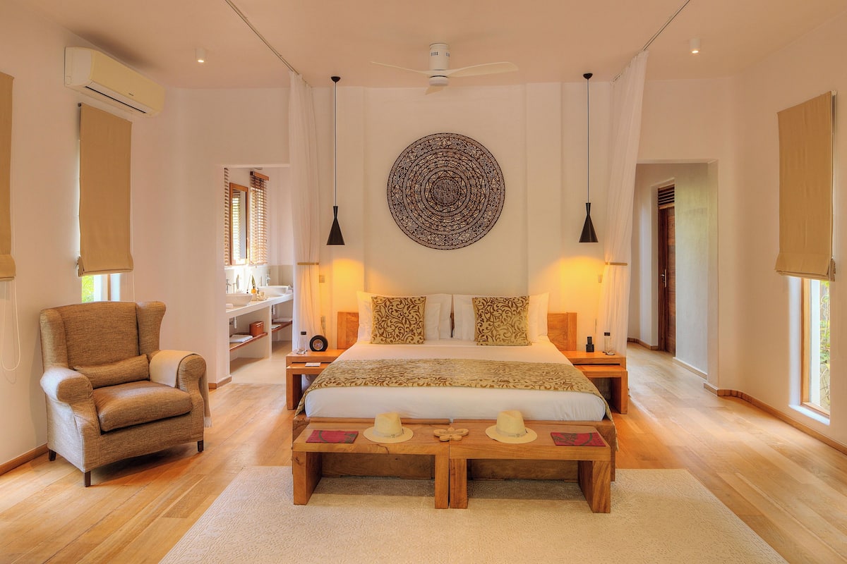 A spacious bedroom with a large bed, bedside tables, a chair, and a decorative wall piece.