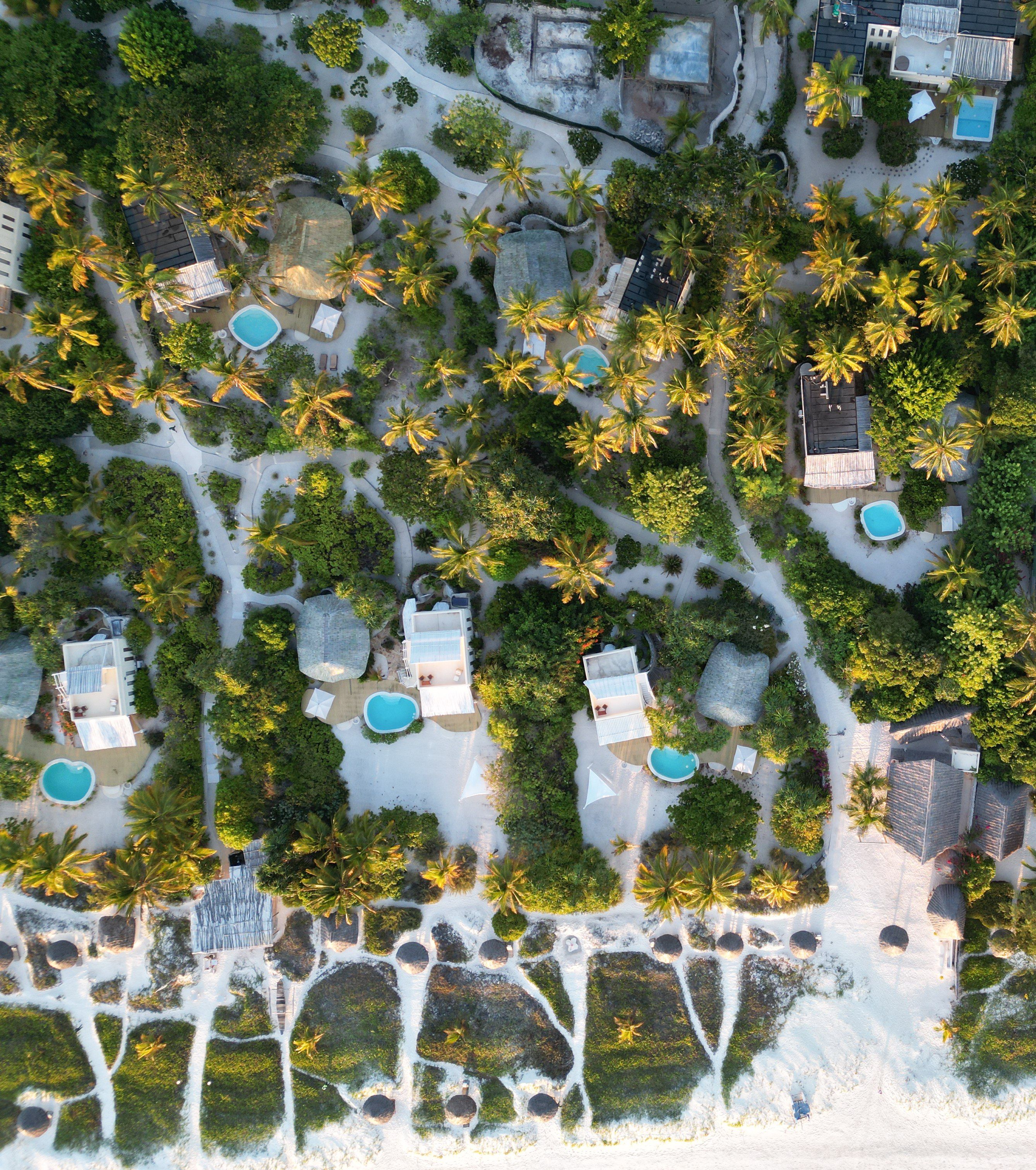 An aerial view of a resort with multiple swimming pools, palm trees, and a beach area.