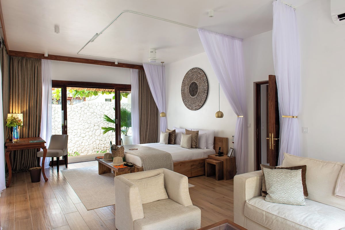 A spacious bedroom with a large bed, a sitting area with a sofa and armchairs, and a dining area with a table and chairs.