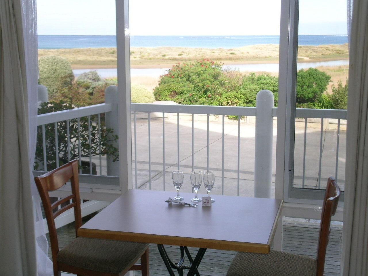 A balcony with a table and chairs, overlooking a beach and ocean.