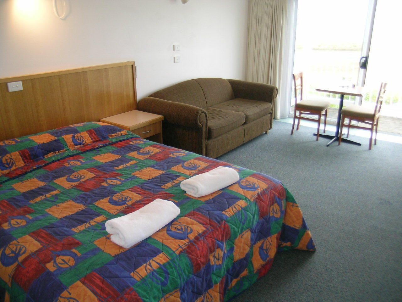 A hotel room with a large bed, a sofa, a small table, and a view of the outdoors.