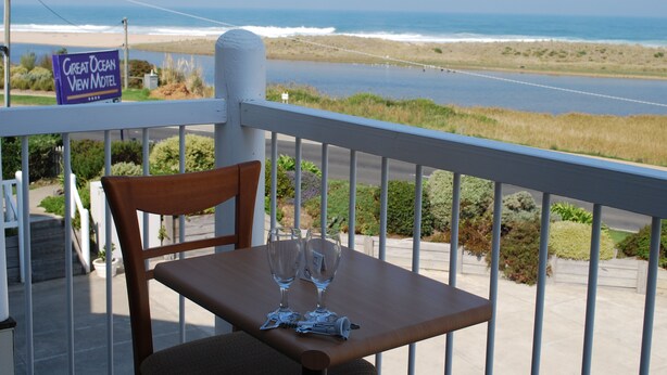 Ein Tisch mit zwei leeren Weingläsern und einem Flaschenöffner auf einem Balkon mit Blick auf einen Strand. Ein Schild des Great Ocean View Motel ist sichtbar.