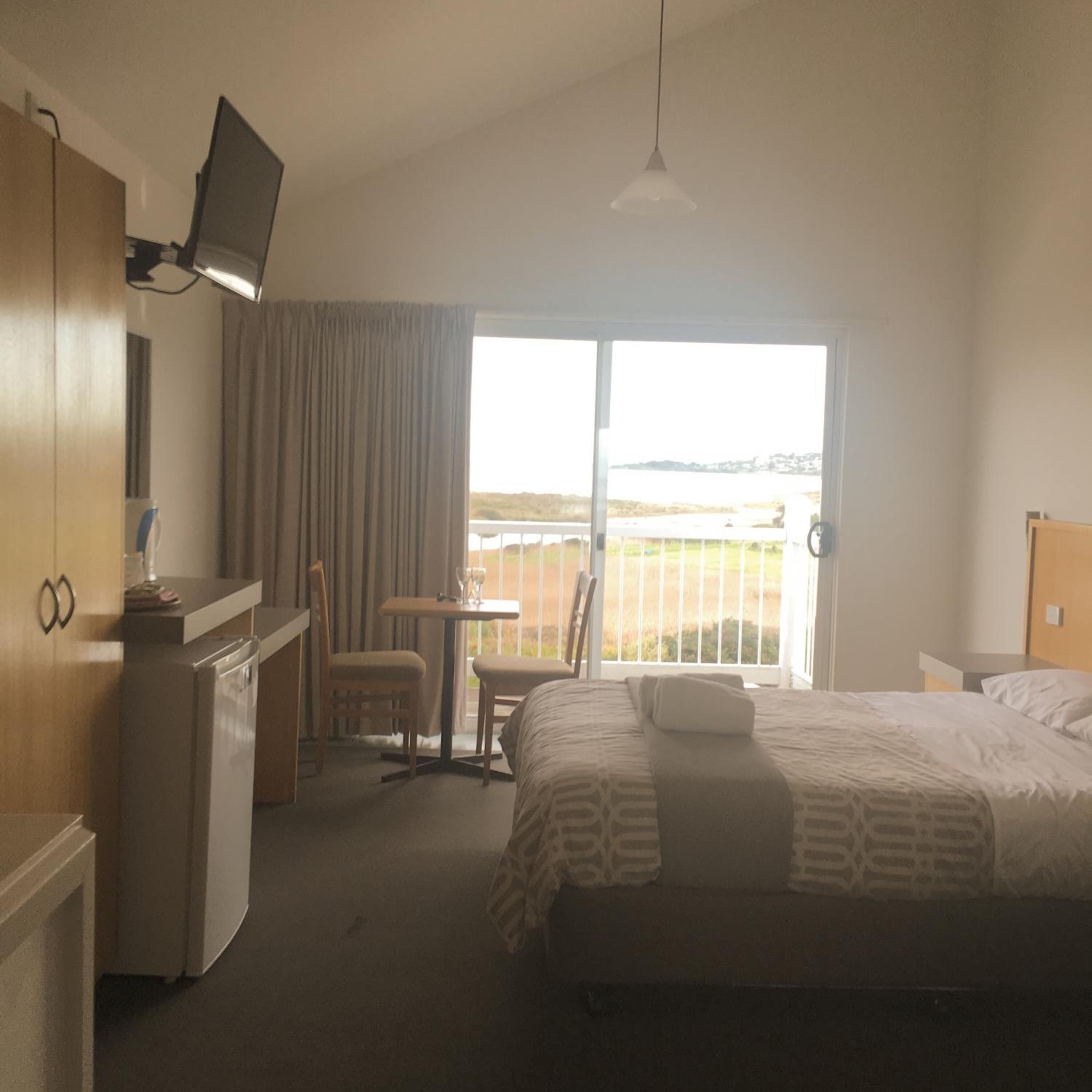 Een hotelkamer met een bed, een bureau, een stoel, een televisie en uitzicht op het strand.
