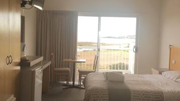 Ein Hotelzimmer mit Bett, Schreibtisch, Stuhl, Fernseher und Blick auf den Strand.