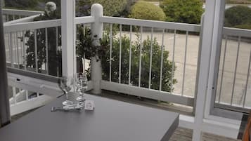 Un balcón con mesa y sillas, con vistas a un paisaje costero con árboles y el mar.